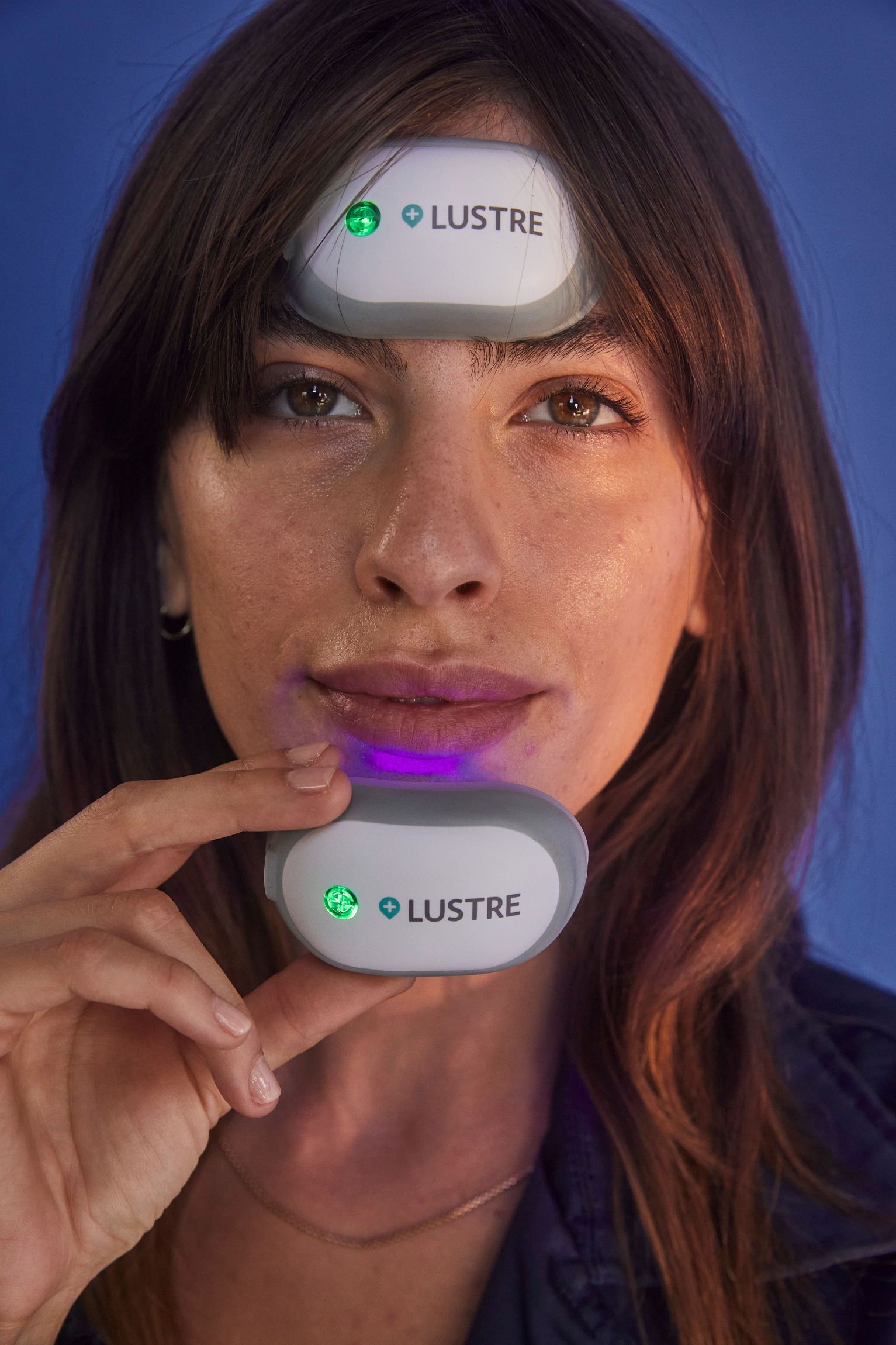 Woman using a LUSTRE device on her face with a blue background